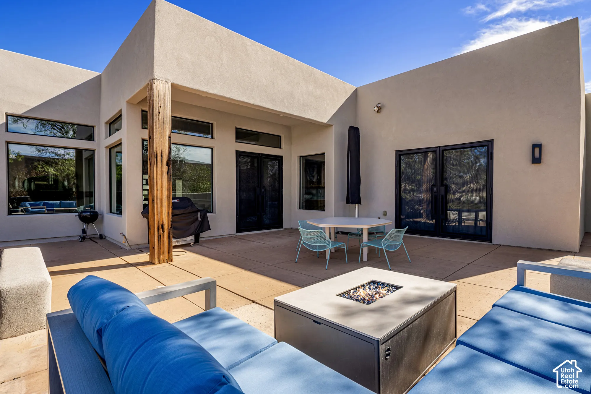 Expansive concrete patio with a modern fire pit, large multi-pane windows, and black frame French doors