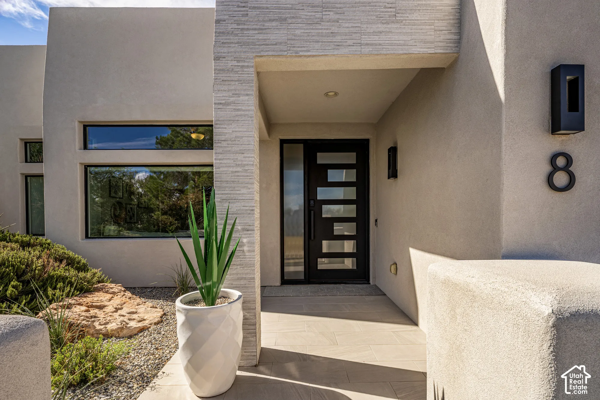 Stucco exterior with a textured stone accent wall, contemporary black entry door with frosted glass panels, and exterior wall sconces