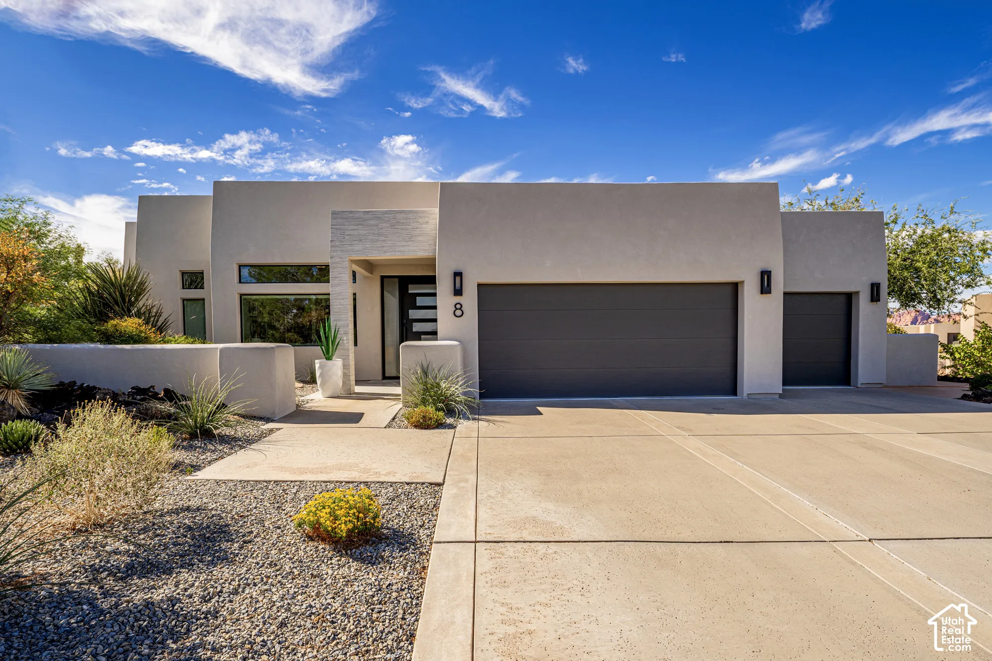 Contemporary stucco exterior with a multi-car garage, concrete driveway, and desert-inspired landscaping