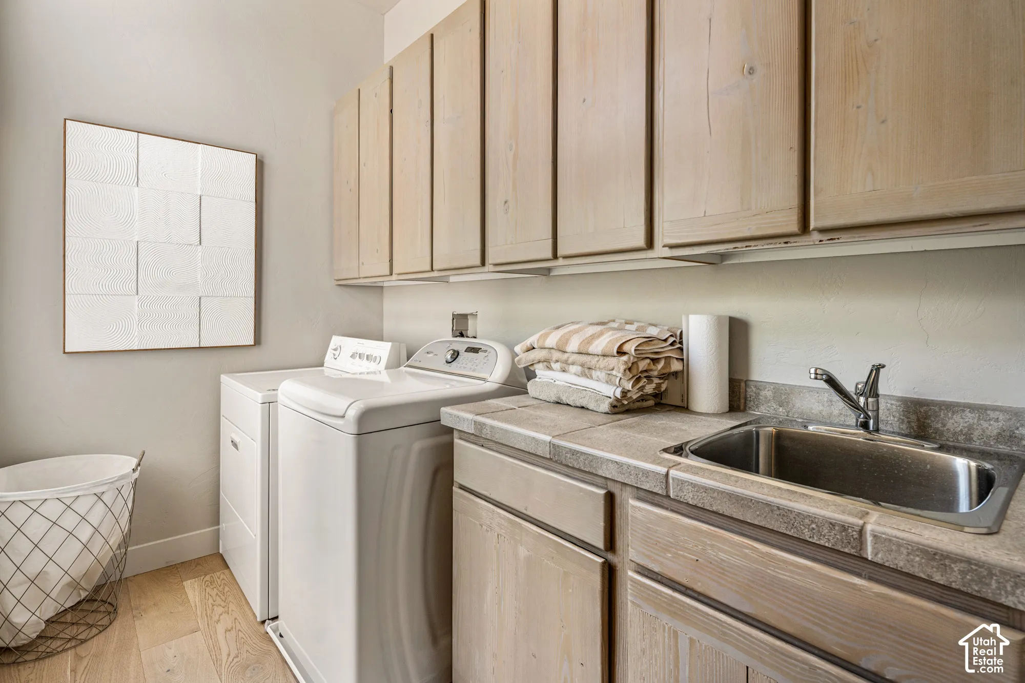 Utility room featuring wood-finish flooring, light-toned cabinetry, a stainless steel sink, and a tiled countertop