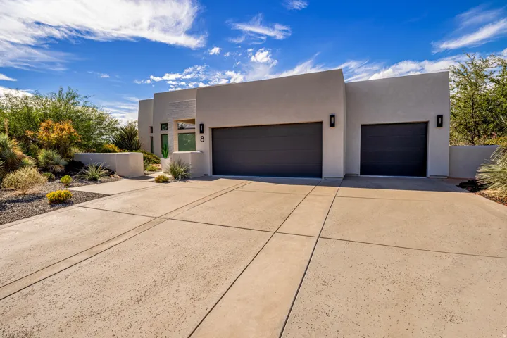 Modern stucco exterior with a multi-car garage, mature desert landscaping, and integrated exterior lighting