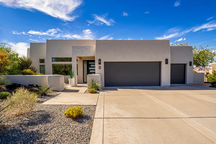 Contemporary stucco exterior with a multi-car garage, concrete driveway, and desert-inspired landscaping