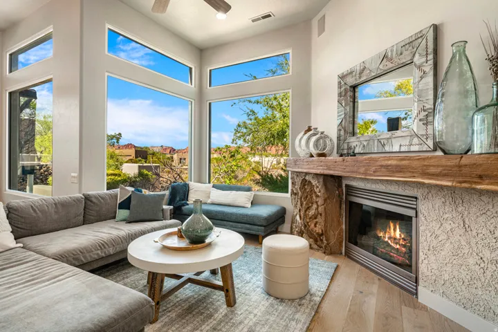 Expansive window array, wood-finish flooring, recessed lighting, ceiling fan, and a fireplace with a rough-hewn stone mantel