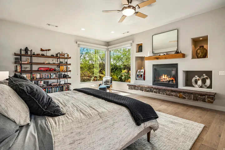 Corner windows, wood-finish flooring, built-in shelving, ceiling fan, and a fireplace with a stone-clad hearth