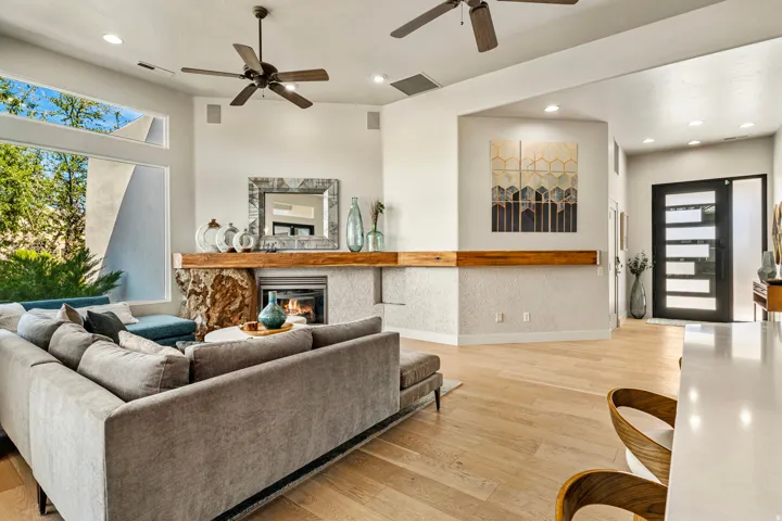 Light wood-finish flooring, stone-clad fireplace with wood mantle, modern dark-frame entry door with frosted glass, recessed lighting, and ceiling fans