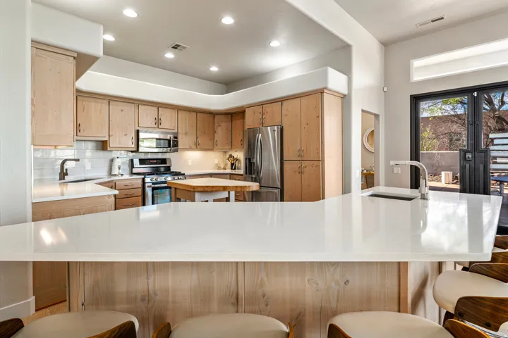 Kitchen featuring light wood cabinetry, stainless steel appliances, a white subway tile backsplash, and a large white countertop with an integrated sink