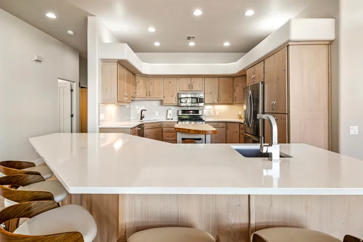 Kitchen featuring recessed lighting, a built-in stainless steel refrigerator, light wood-finish cabinetry, a large kitchen island with an undermount sink, and white countertops