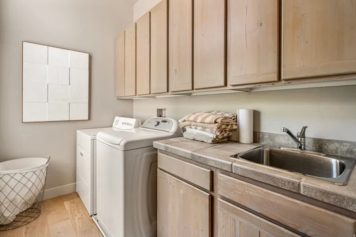 Utility room featuring wood-finish flooring, light-toned cabinetry, a stainless steel sink, and a tiled countertop