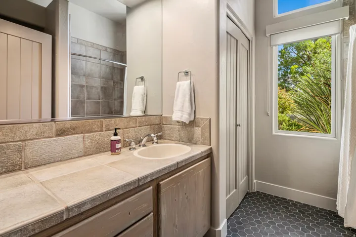 Vanity with tile countertop, integrated sink, and wood-finish cabinetry