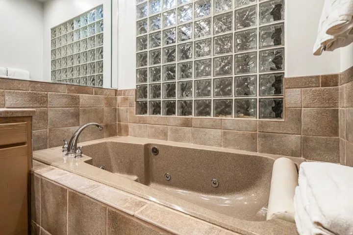 Soaking tub with jetted features, chrome fixtures, and surrounding tilework