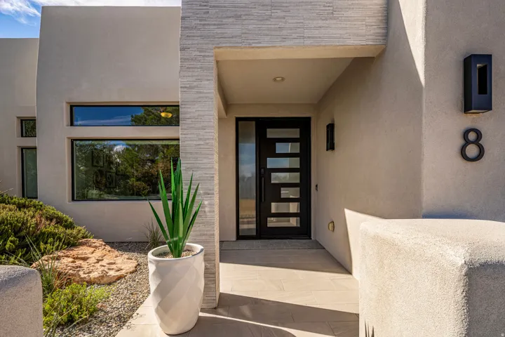 Stucco exterior with a textured stone accent wall, contemporary black entry door with frosted glass panels, and exterior wall sconces