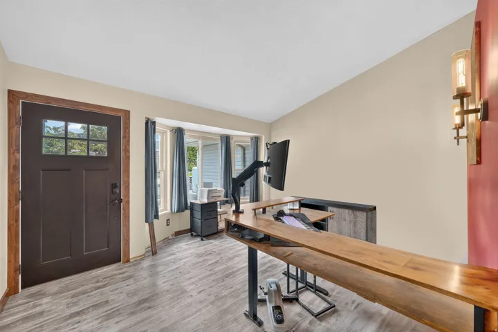 Entry door with upper glass panes and wood-finish trim, bay window with multiple panes, wood-finish flooring, and a wall-mounted sconce light fixture