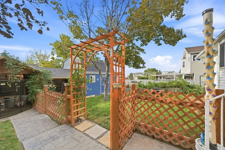 Gated backyard entrance featuring a wooden arbor, lattice fencing, and a blue storage shed
