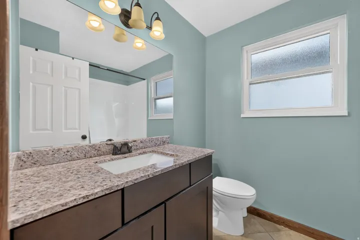 Bathroom featuring a dark wood-finish vanity with an integrated sink, a speckled countertop, tile flooring, and a window with privacy glass