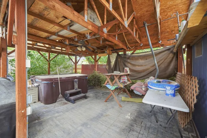 Covered outdoor area featuring exposed wood beam construction, a built-in spa, and a ceiling fan