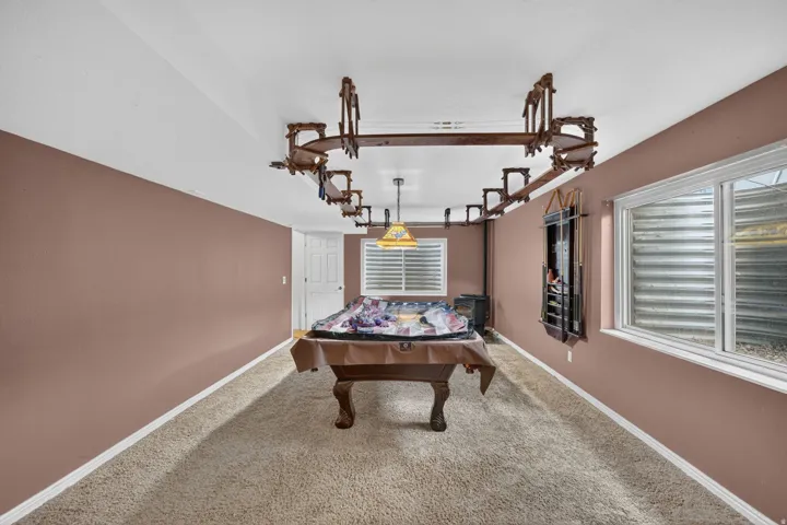 Spacious room featuring neutral carpeting, a wood-finish pool table, and window with horizontal blinds