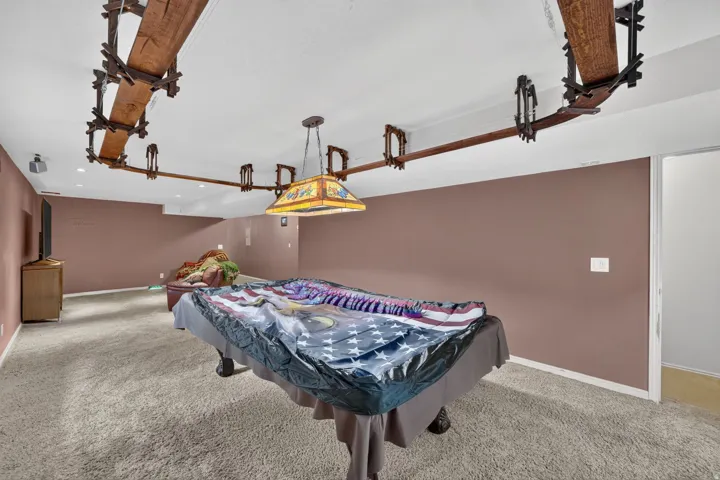 Expansive recreation room featuring a suspended wooden track light fixture, recessed ceiling lights, and carpeted flooring