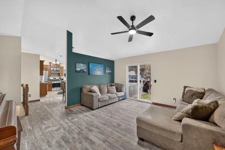 Vaulted ceiling, ceiling fan with integrated lighting, wood-finish flooring, sliding glass door, and a built-in kitchen featuring stainless steel appliances