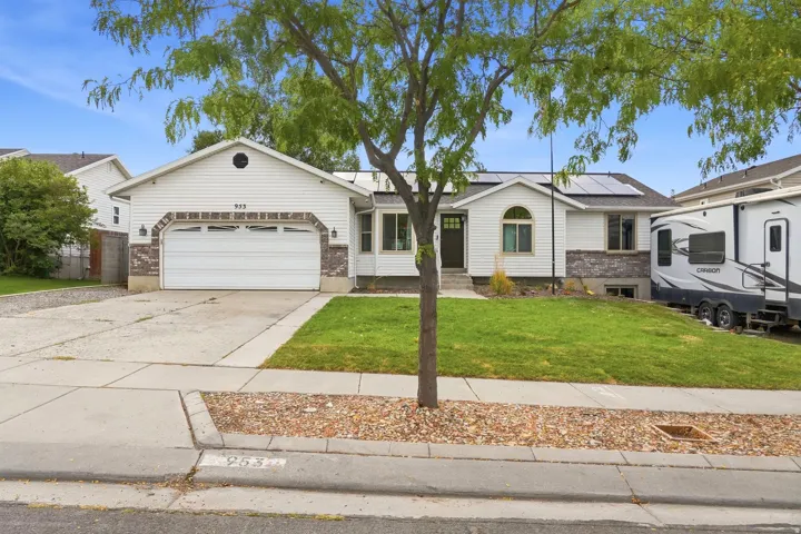 White siding exterior with a stone veneer accent, attached garage, solar panels, and a front lawn with mature landscaping