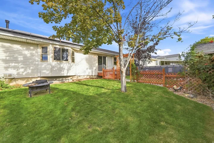 Expansive green lawn, white vinyl siding, rear wood deck, wood lattice fencing, and mature trees