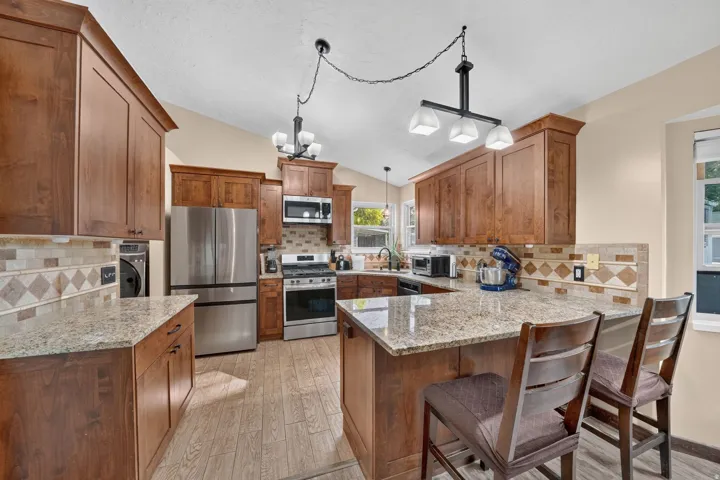 Kitchen featuring wood-finish cabinetry, stainless steel appliances, granite countertops, and a decorative tile backsplash