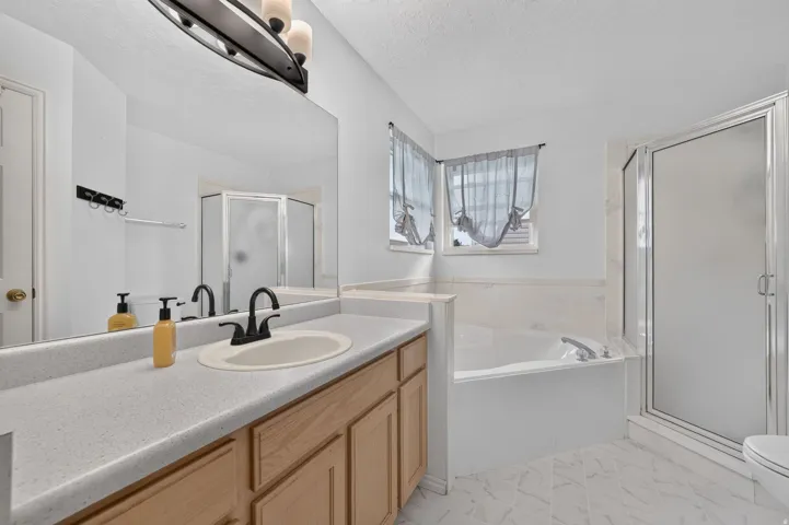 Bathroom featuring a built-in soaking tub, glass-enclosed shower, wood-finish vanity with a single sink, and a large wall-mounted mirror