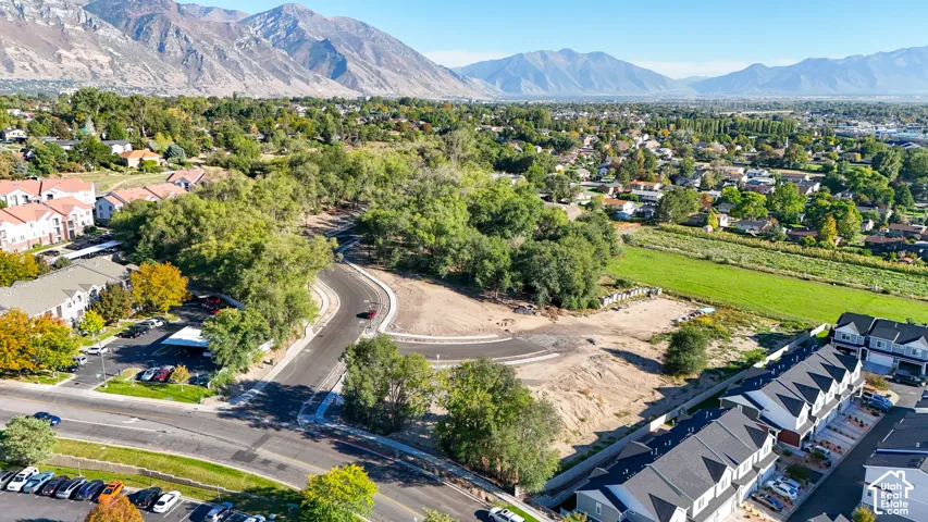 Expansive mountain range backdrop, established neighborhood with mature trees, new townhome construction, undeveloped land parcel, paved roadways