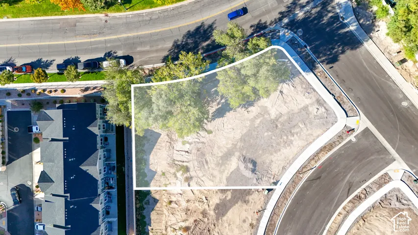 Aerial view of a vacant lot, featuring defined property boundaries, adjacent paved roads, and established street-side landscaping