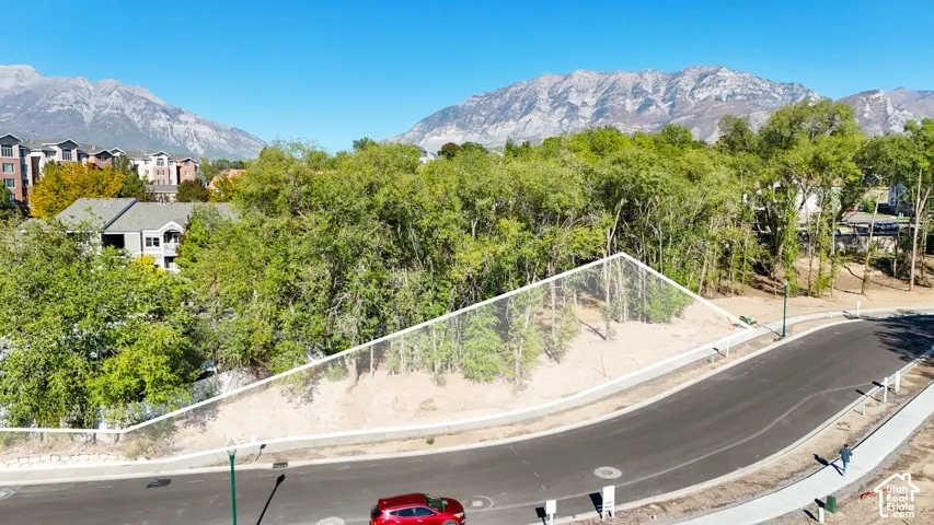 Mountain backdrop with mature trees, paved road, and concrete sidewalks