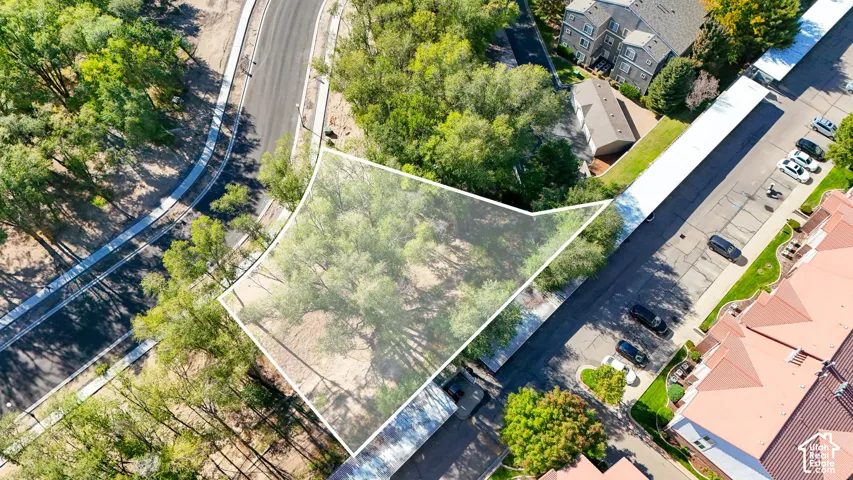 Treelined parcel featuring a defined boundary, adjacent to paved roadways, with nearby residential structures