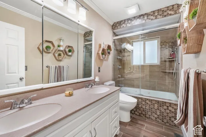 Dual vanity with integrated sinks, full-width mirror, glass-enclosed shower over tub, tiled tub surround, and wood-finish flooring