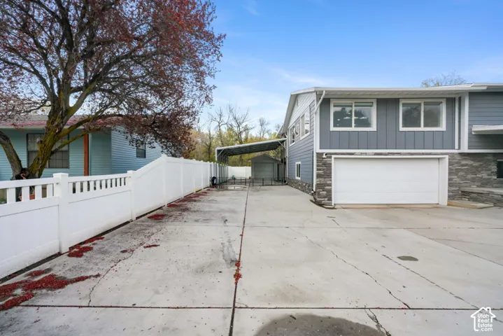 Concrete driveway with a white privacy fence and an attached carport