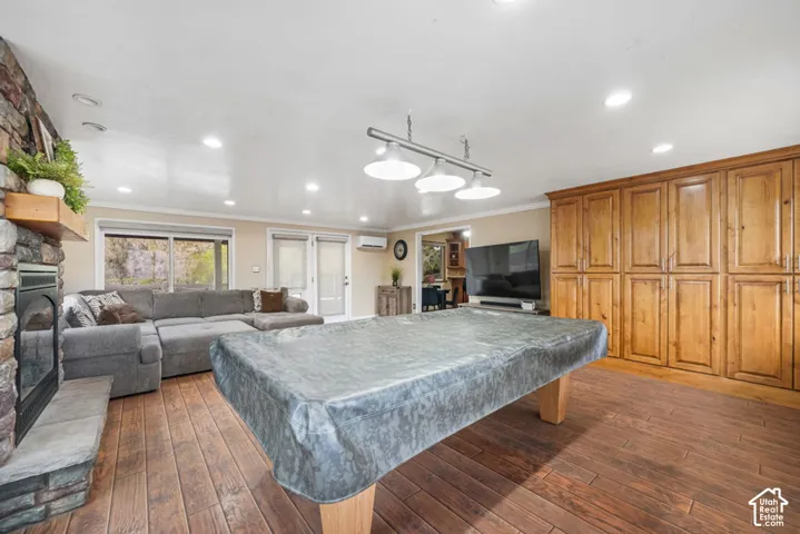 Spacious Pool Table REC room featuring wood-finish flooring, a stone-clad fireplace with a hearth, extensive wood-paneled cabinetry, recessed lighting, and a multi-light fixture