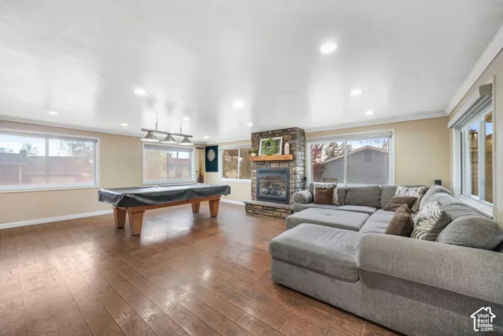 Expansive room featuring wood-finish flooring, a stone-clad fireplace with a wood mantle, recessed lighting, and multiple windows