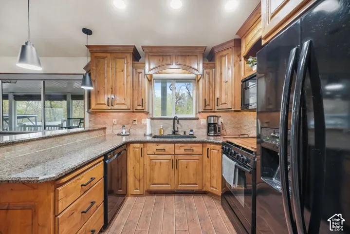 Wood-finish flooring, wood cabinetry with upper and lower storage, stone countertops, and a tiled backsplash