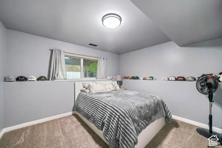 Bright secondary bedroom down stairs, with carpet flooring, large window with natural light, ceiling-mounted light fixture, and built-in shelving along the upper walls