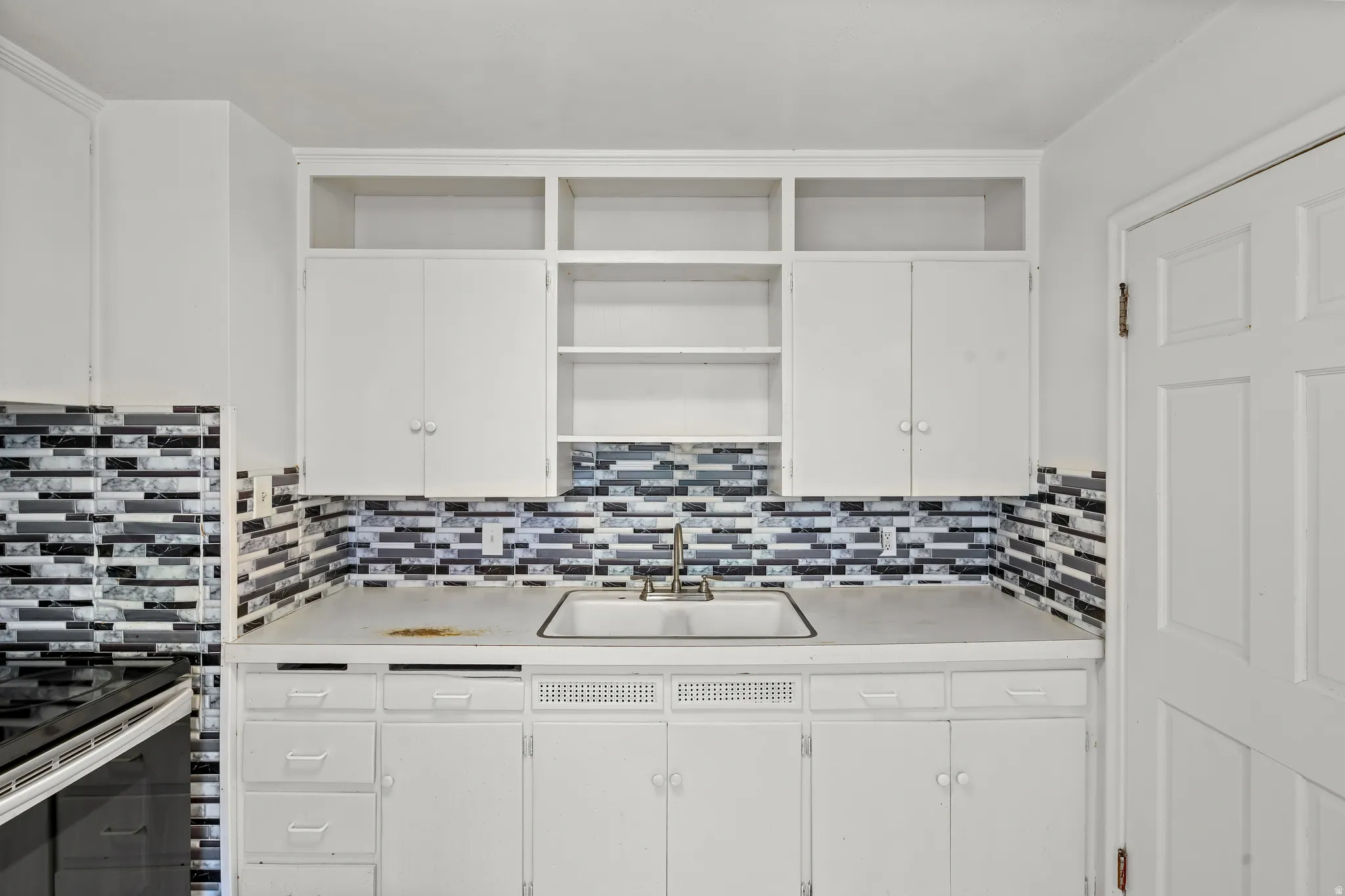 White cabinetry and open shelving with a dual basin sink, white countertop, and tiled backsplash