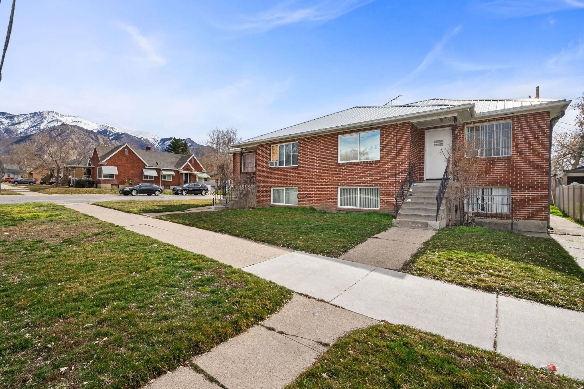 Brick exterior with a metal roof, concrete walkway, and snow-capped mountain backdrop