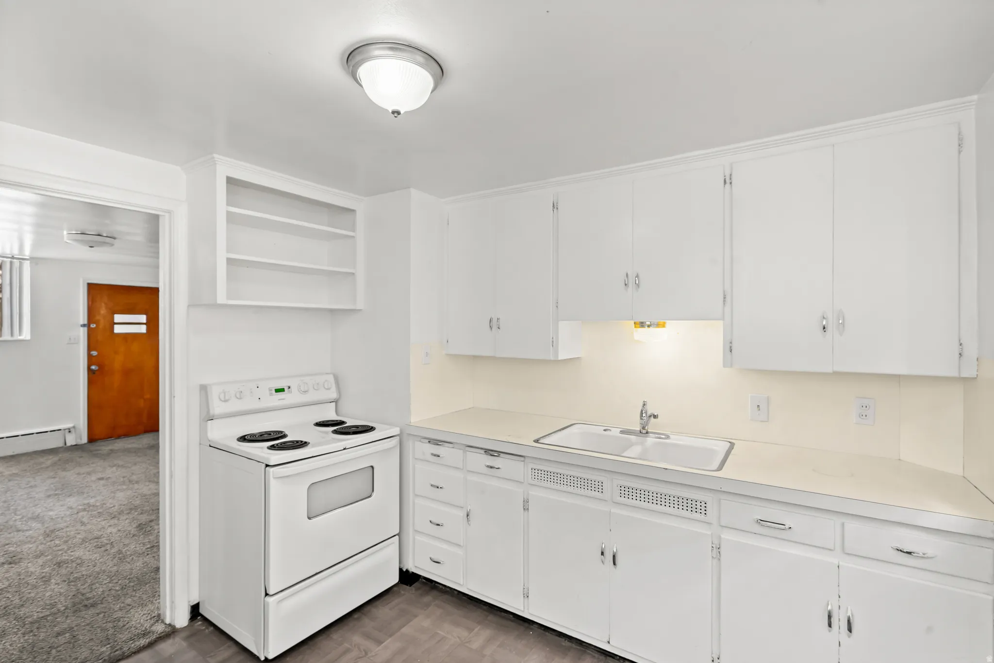 White cabinetry, integrated range, white countertop, double basin sink, and wood-finish flooring