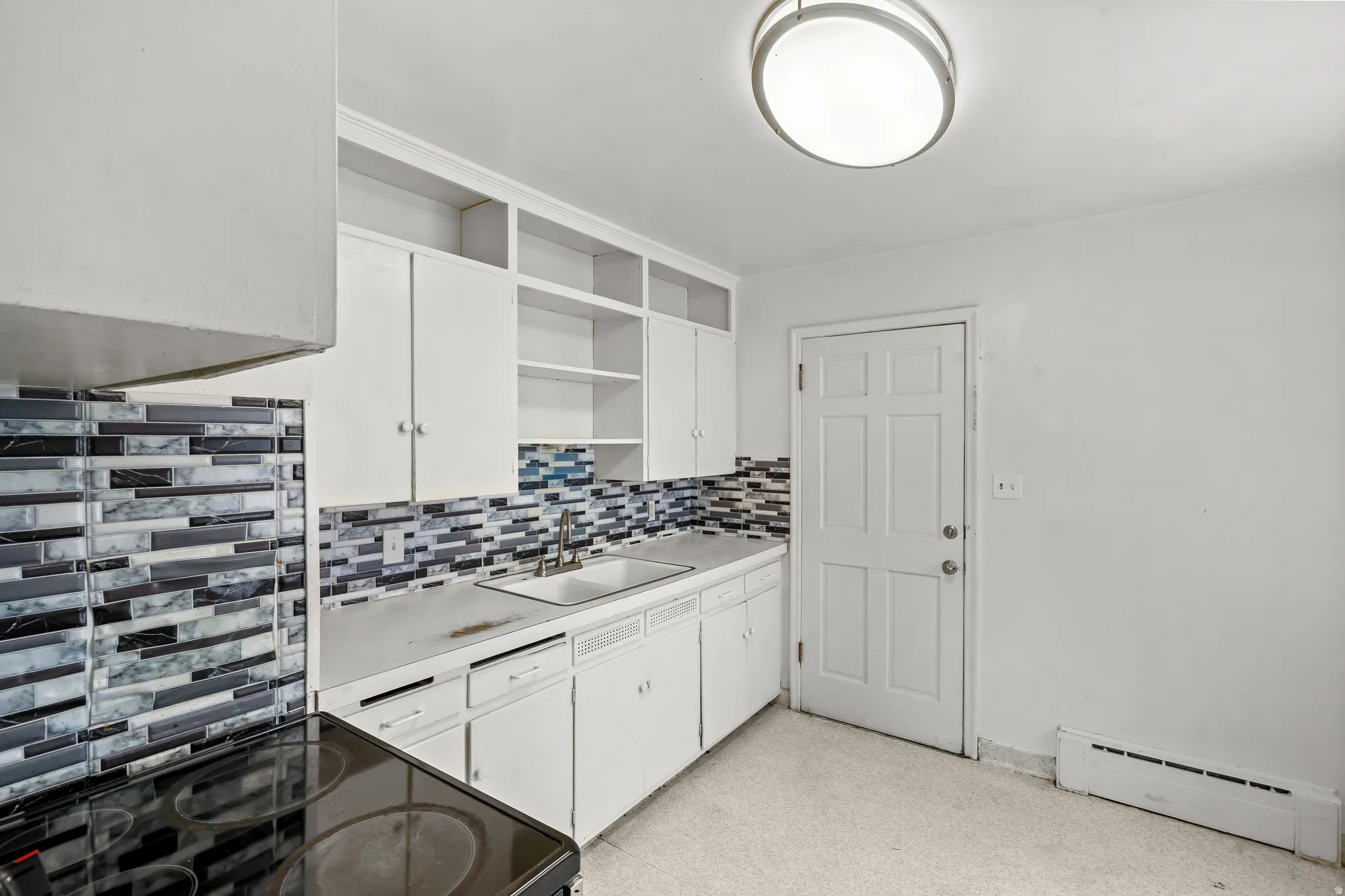 White cabinetry with open shelving, mosaic tile backsplash, solid surface countertops, and an integrated sink