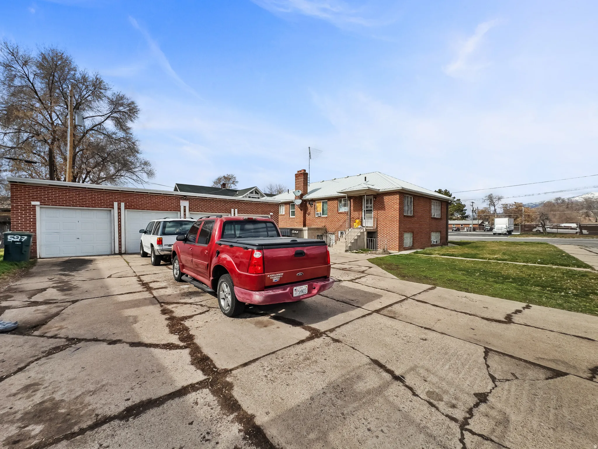 Brick exterior residence with a multi-car garage, mature trees, and a paved driveway