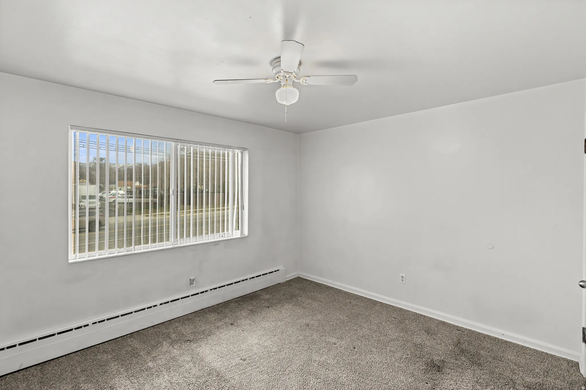 Wall-to-wall carpeting, a horizontal window with vertical blinds, and a ceiling fan with integrated lighting