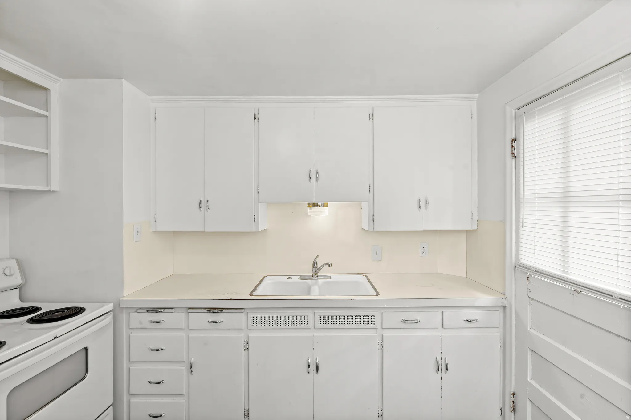 White cabinetry, white countertop, double basin sink, built-in shelving, and a window with blinds