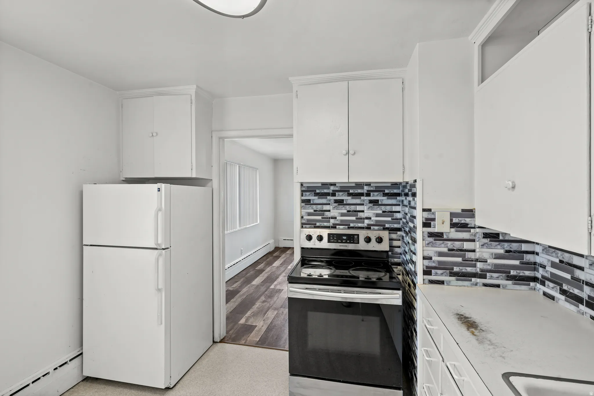 Kitchen featuring white cabinetry, a mosaic tile backsplash, white appliances, and wood-finish flooring visible in the adjacent room