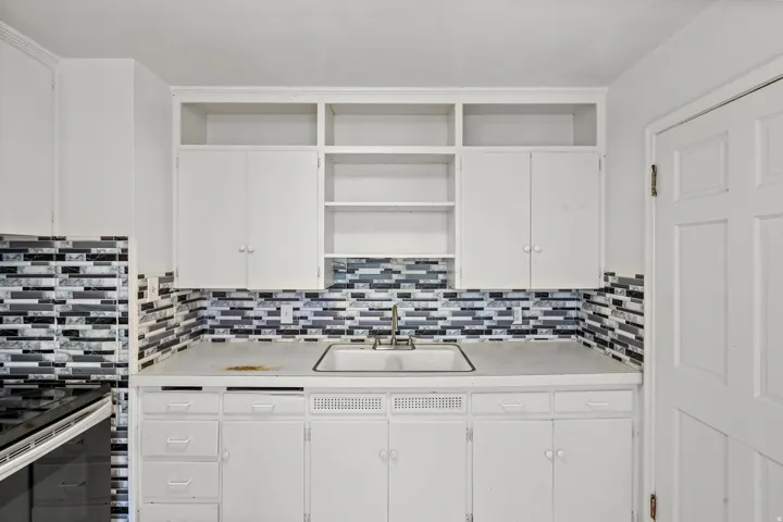 White cabinetry and open shelving with a dual basin sink, white countertop, and tiled backsplash