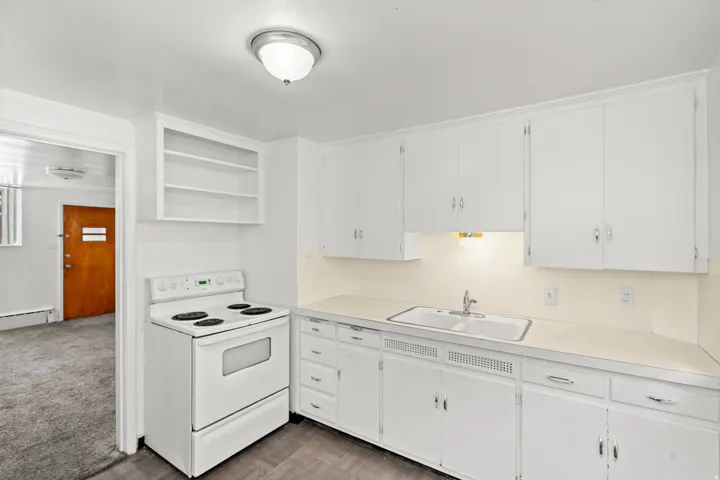 White cabinetry, integrated range, white countertop, double basin sink, and wood-finish flooring