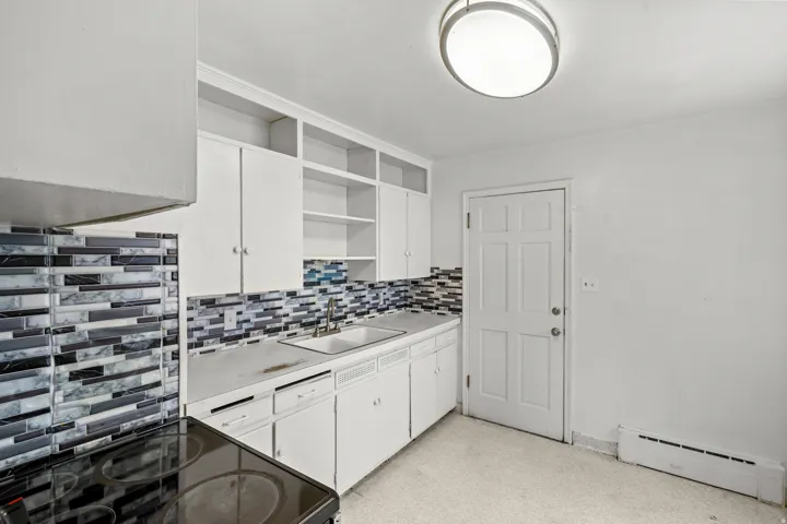 White cabinetry with open shelving, mosaic tile backsplash, solid surface countertops, and an integrated sink