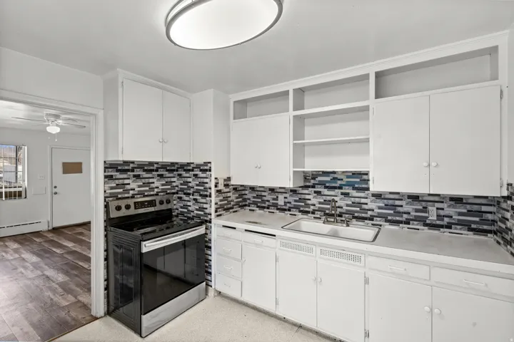 Kitchen featuring white cabinetry, a stainless steel range, a mosaic tile backsplash, and a double basin sink