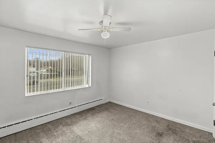 Wall-to-wall carpeting, a horizontal window with vertical blinds, and a ceiling fan with integrated lighting