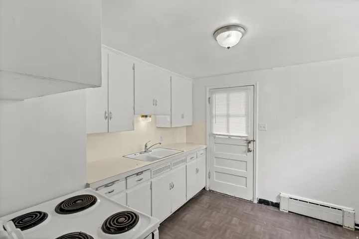 White cabinetry with brushed nickel hardware, dual basin sink, integrated countertop, and wood-finish flooring